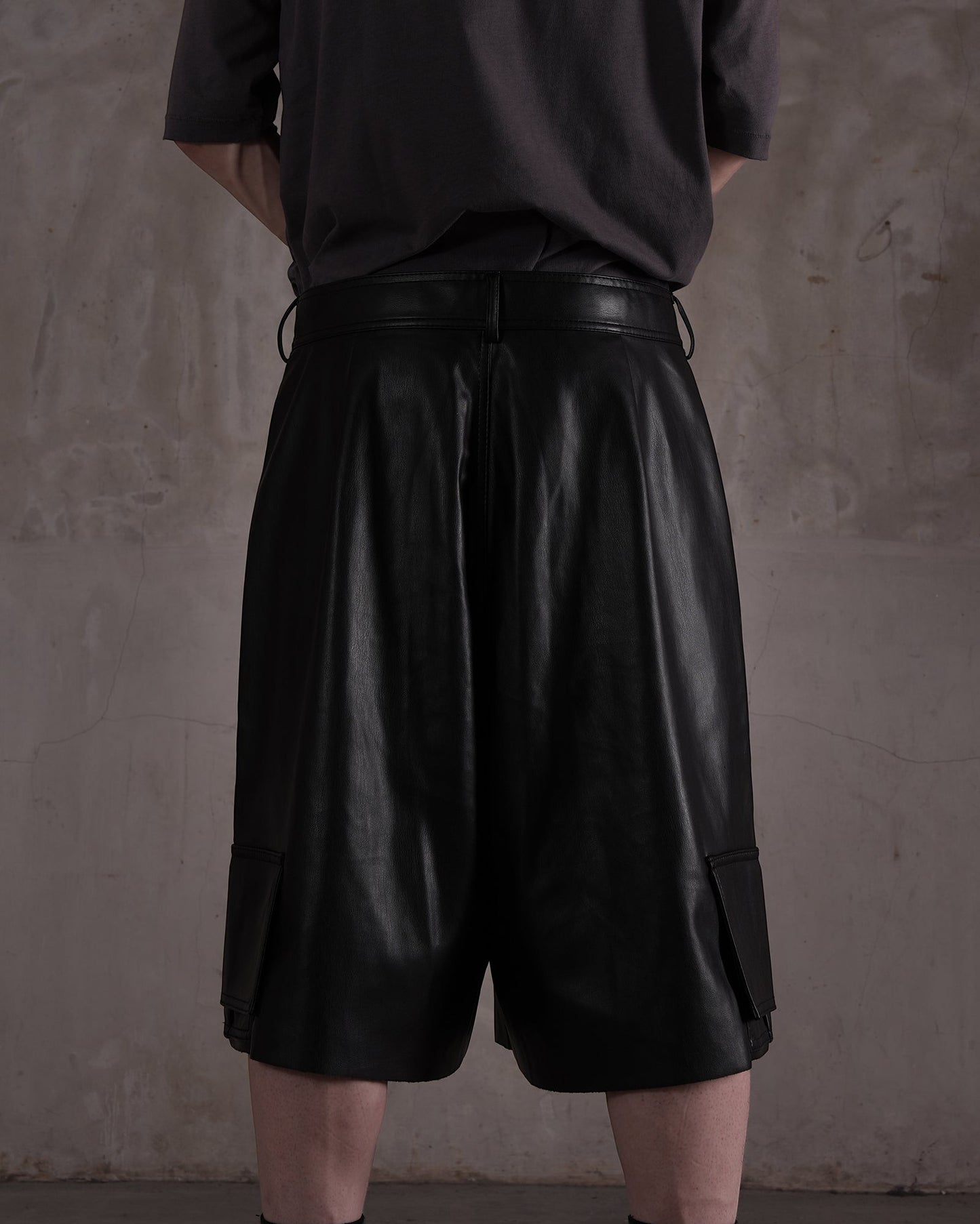 KYOHEY_FUJITAの黒いレザー製デコンストラクトハーフパンツ。ゆったりとしたシルエットでサイドポケット付きの背面ビュー。