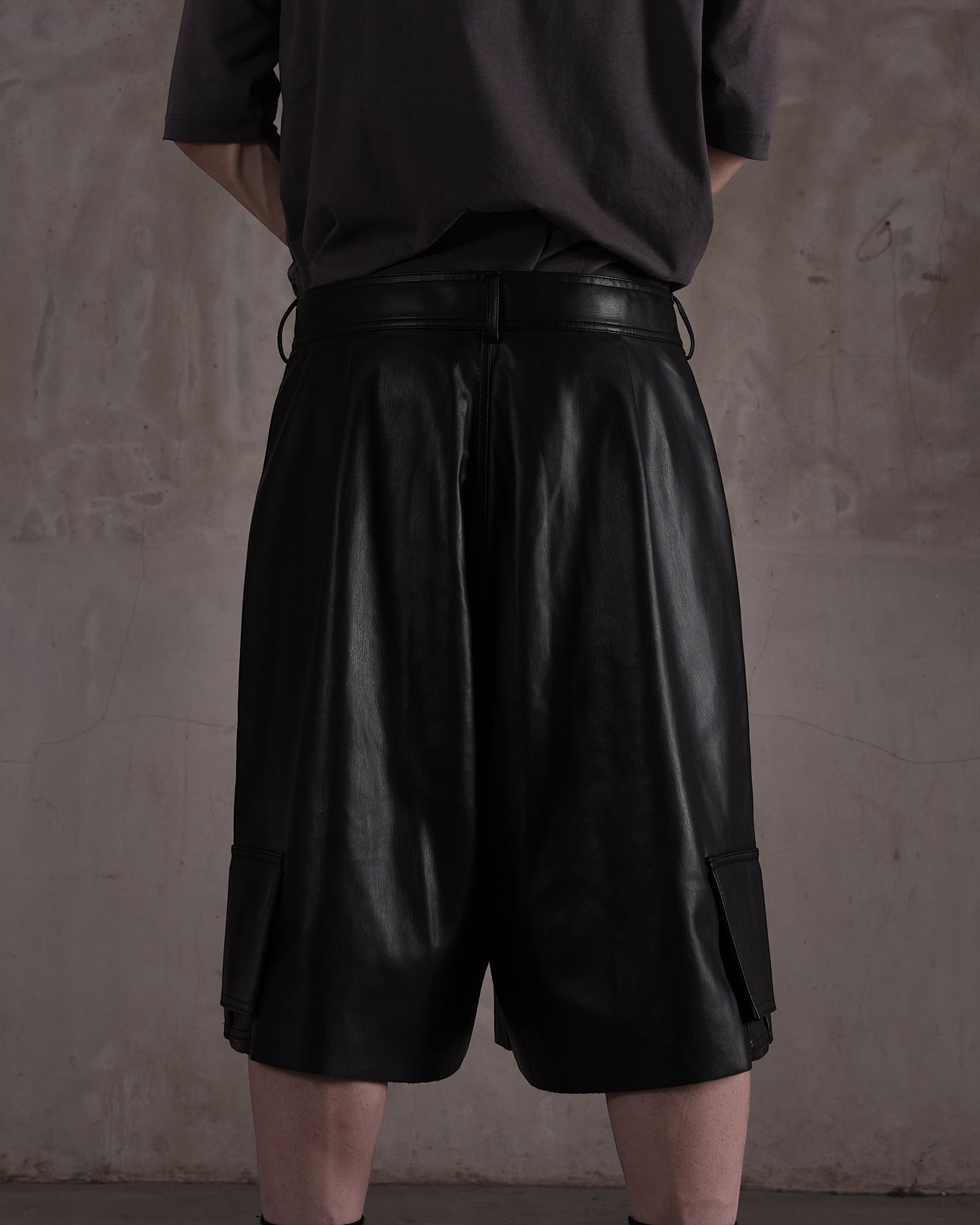 KYOHEY_FUJITAの黒いレザー製デコンストラクトハーフパンツ。ゆったりとしたシルエットでサイドポケット付きの背面ビュー。