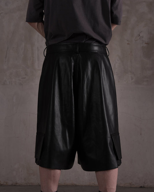 KYOHEY_FUJITAの黒いレザー製デコンストラクトハーフパンツ。ゆったりとしたシルエットでサイドポケット付きの背面ビュー。