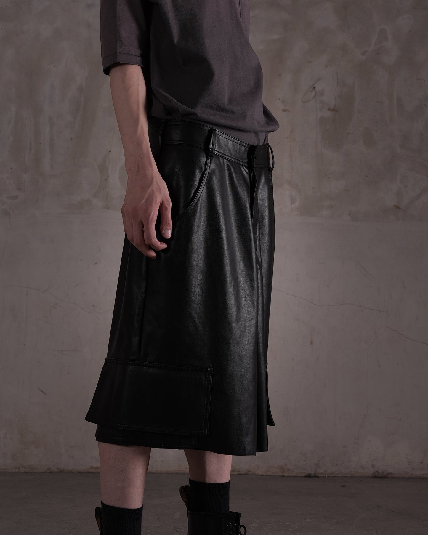 KYOHEY_FUJITAの黒いレザー製ハーフカットショートパンツ。デコンストラクトなデザインとサイドポケットが特徴的な膝丈のボトムス。