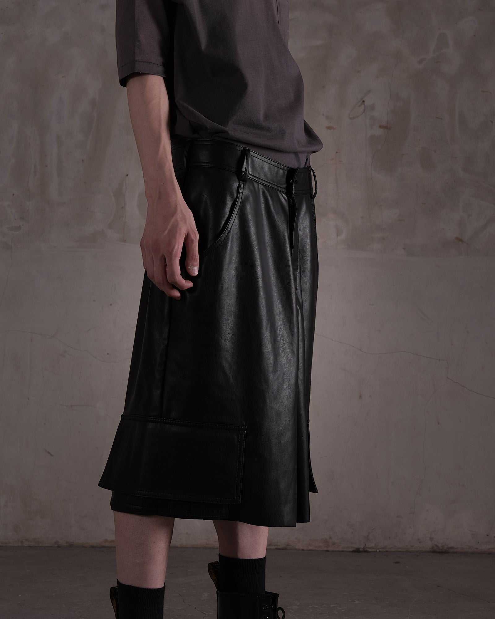 KYOHEY_FUJITAの黒いレザー製ハーフカットショートパンツ。デコンストラクトなデザインとサイドポケットが特徴的な膝丈のボトムス。
