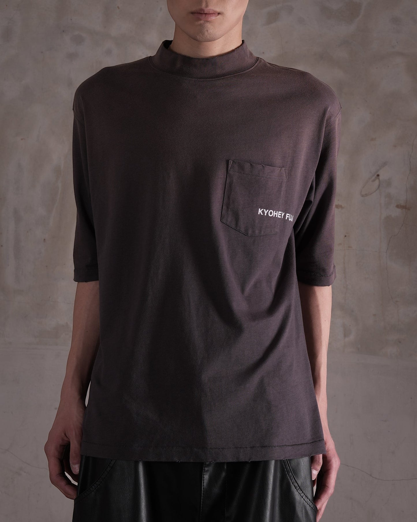 KYOHEY_FUJITAのヘビーウォッシュ加工されたダークブラウンのモックネックロゴTシャツ。胸ポケットにブランドロゴ入り。