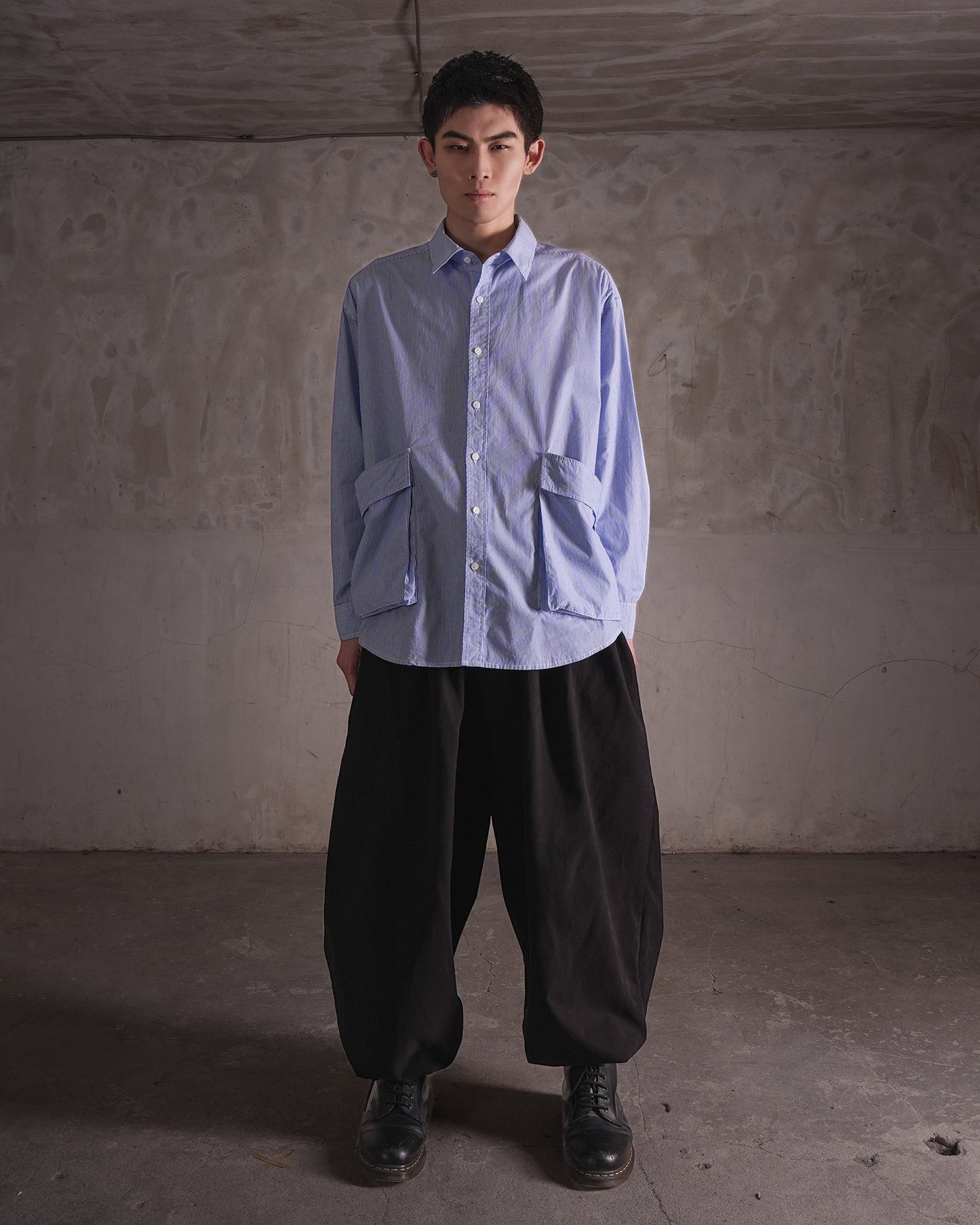KYOHEY_FUJITAのオーバーサイズなストライプ柄シャツ。前面に大きなポケットが2つ付いたデコンストラクトデザインで、黒のワイドパンツと合わせています。