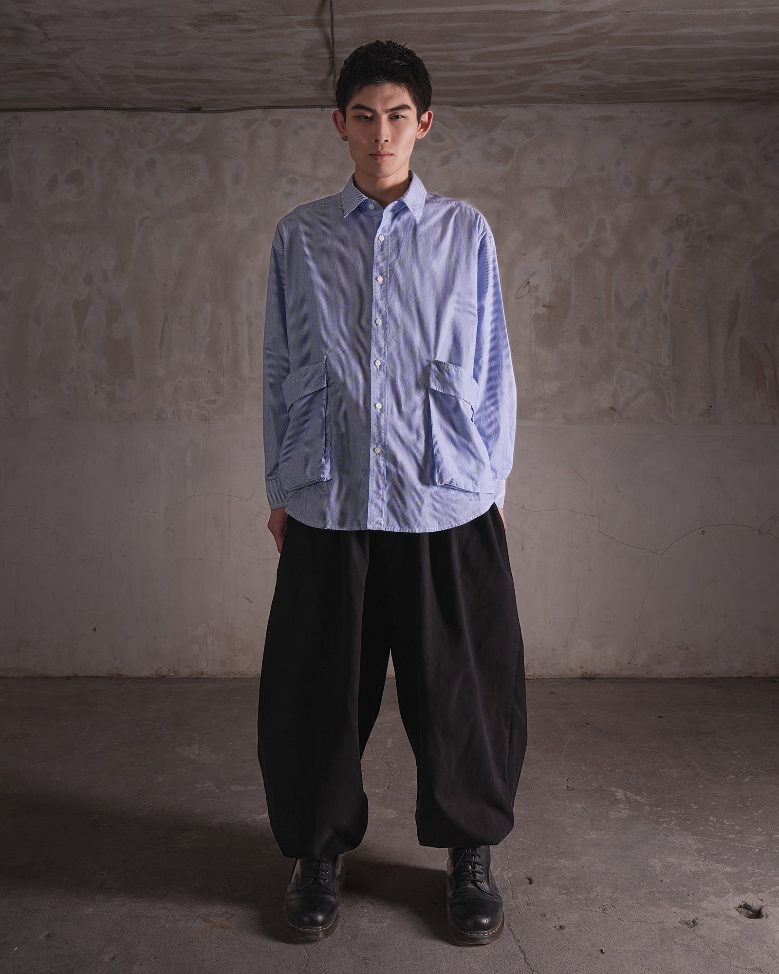 KYOHEY_FUJITAのオーバーサイズなストライプ柄シャツ。前面に大きなポケットが2つ付いたデコンストラクトデザインで、黒のワイドパンツと合わせています。