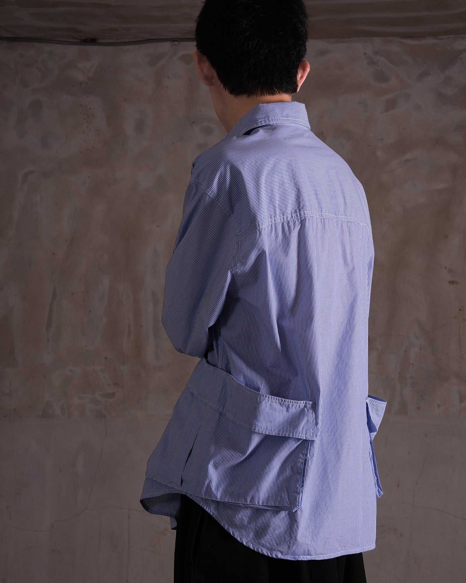 KYOHEY_FUJITAのブルーのストライプ柄オーバーサイズシャツ。背面に複数のポケットが付いたデコンストラクトデザイン。