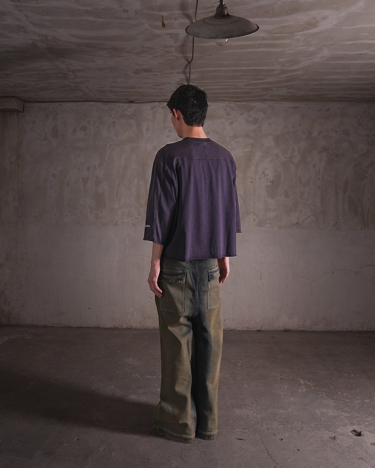 KYOHEY_FUJITAのヴィンテージ加工されたダークパープルのクロップド丈ロゴTシャツを着用した男性の背面ショット
